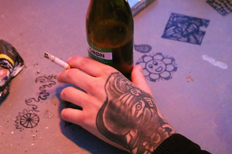 closeup of a tattooed hand holding a cigarette and beer